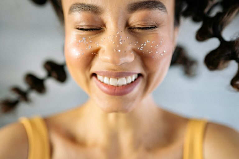 Smiling young woman with curly hair and glitter in a close-up portrait.