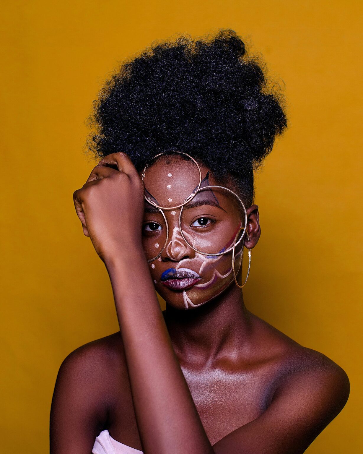Artistic portrait of a woman with unique face paint against a vibrant backdrop.